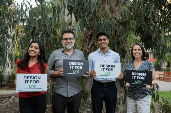 four speakers stand with signs reading "Design it for us" outside of the Haas Center